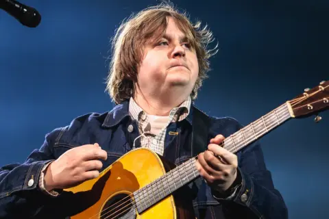Lewis Capaldi gra na gitarze, mimo swojej choroby, z pasją i zaangażowaniem.
