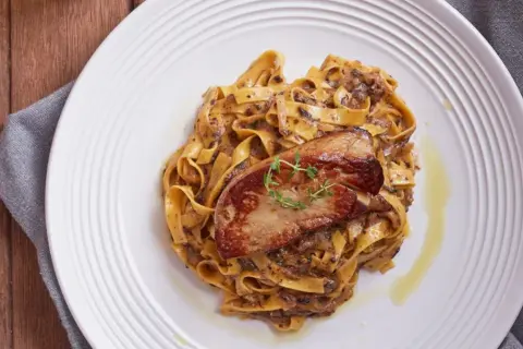 Pasta con foie gras, un plato gourmet con un trozo dorado de foie gras sobre una cama de fettuccine cremoso.