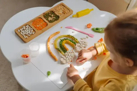 Dziecko tworzy tęczę z plasteliny i ziaren. Wspaniałe zabawy sensoryczne rozwijają kreatywność.