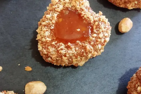 Un sablé algérien à la confiture, enrobé de noisettes concassées, sur fond sombre.