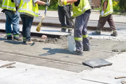 Prace interwencyjne: robotnicy w kamizelkach odblaskowych wylewają beton na torowisko.