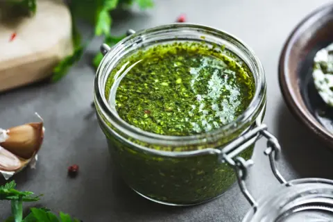 Słoik domowego pesto z bazylii, obok czosnek i świeże zioła. Idealne do makaronu.