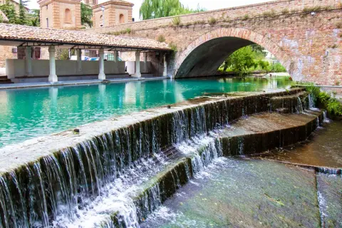 Cascata d'acqua cristallina sotto un antico ponte in mattoni, un angolo di pace tra i borghi medievali umbri.