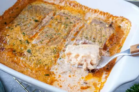 Saftiges Lachsfilet in cremiger Sahnesauce, ein köstliches Lachs Sahne Gratin, wird mit einer Gabel herausgehoben.