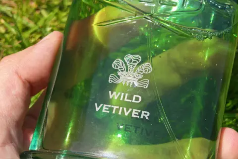Zielona butelka perfum Creed Wild Vetiver w dłoni na tle trawy.