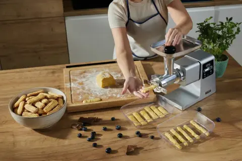 Przygotowywanie kruche ciasteczka do długiego przechowywania. Maszyna do ciastek formuje paski ciasta, które trafiają do pojemników.