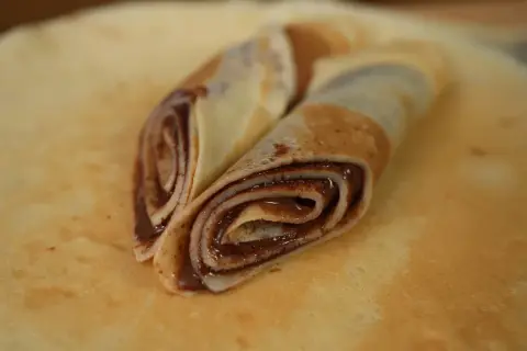 Zwei gerollte low carb pfannkuchen mit Schokoladencreme, auf einem größeren Pfannkuchen liegend.