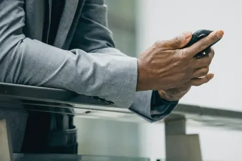 Mężczyzna w szarej marynarce i spodniach, trzymający telefon. Idealny zestaw: jaka marynarka do szarych spodni?