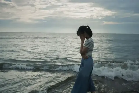 Kobieta na plaży, zakrywająca twarz dłońmi, symbolizuje objawy depresji.