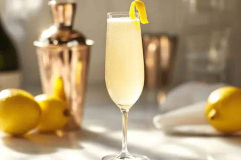 En elegant French 75 med citronskal, bredvid citroner och en kopparskakare.