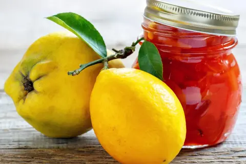 Gelbe Quittenfrucht und Zitrone neben einem Glas mit roter Marmelade.