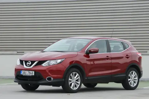 Czerwony Nissan Qashqai J11, z widocznym wykazem żarówek w przednich reflektorach, zaparkowany na tle falistej ściany.