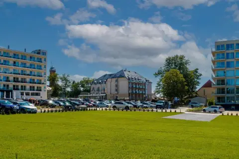 Nowoczesne budynki hotelowe i parking pełen samochodów na tle błękitnego nieba z chmurami.