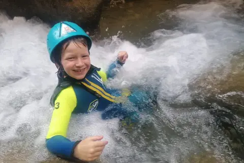 Niño sonriente con casco y traje de neopreno disfrutando del barranquismo en la Sierra de Guara. ¡Una aventura de senderismo acuático inolvidable!