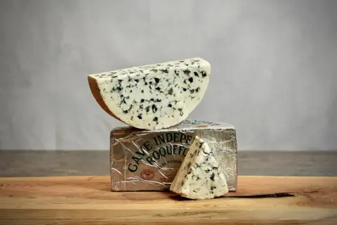 Un morceau de roquefort est posé sur son emballage argenté, avec une autre part en triangle à côté.
