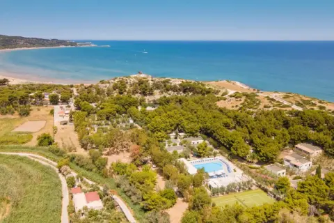 Vista aerea della baia della Tufara con mare azzurro, spiaggia dorata, pineta lussureggiante, piscina e campo da tennis.