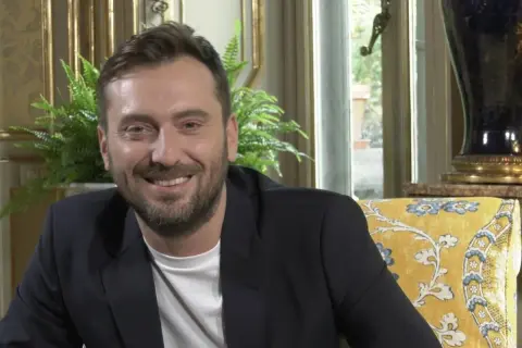 Un uomo sorride, con un blazer scuro e una maglietta bianca. I testi di Cesare Cremonini dicono di me che sono felice.