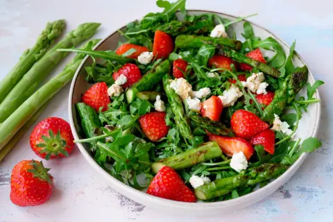 Frischer Spargelsalat mit Erdbeeren und Rucola, garniert mit zerbröseltem Käse.
