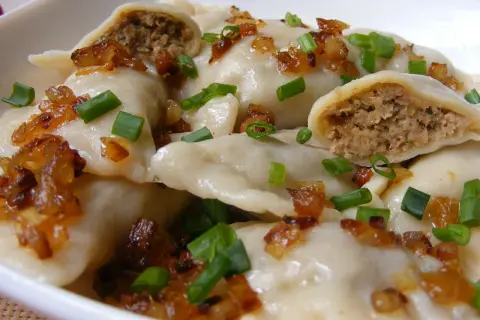 Pyszne pierogi z mięsem, okraszone skwarkami i szczypiorkiem, kuszą swoim domowym wyglądem.