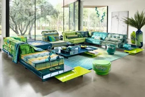 Un salón con sofás modulares en tonos verdes y azules, alfombra degradada y mesas de centro de cristal. Un look boho chic verano perfecto para relajarse.