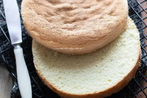 Due dischi di pan di spagna senza glutine, uno sopra l'altro, su una griglia. Un coltello è visibile a sinistra.