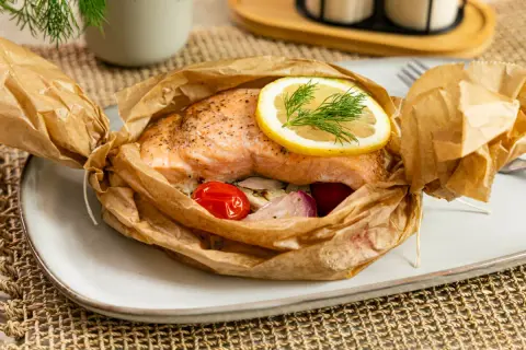 Saftiges Lachsfilet in Alufolie gegrillt, garniert mit Zitrone und Dill, serviert mit Kirschtomaten und Zwiebeln.
