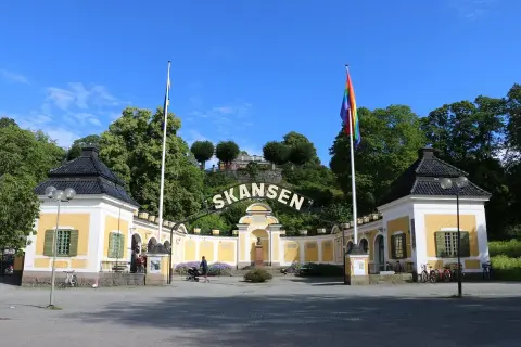 Skansen, Stockholms berömda friluftsmuseum, välkomnar besökare med gula byggnader och en regnbågsflagga.