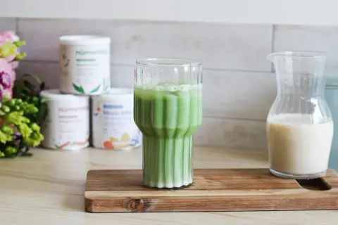 Un verre de matcha chaud, mousseux et crémeux, prêt à être dégusté. À côté, une carafe de lait végétal.