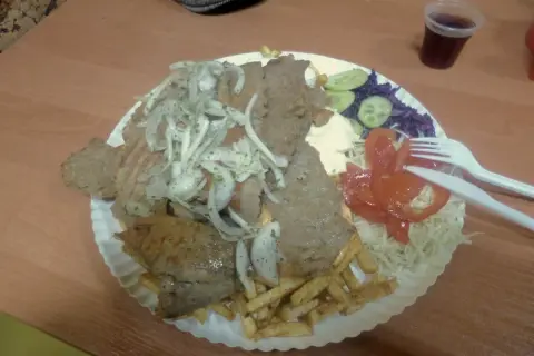 Talerz z kebabem, frytkami, warzywami i napojem.