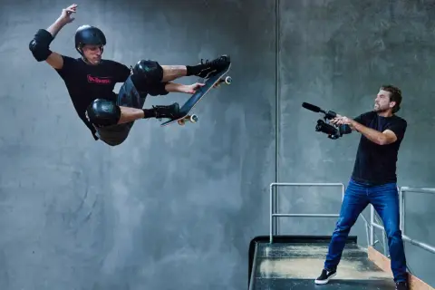Tony Hawk w locie na deskorolce, filmowany przez operatora kamery.