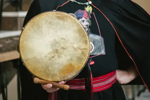 Mateusz Dobrowolski trzyma bębenek. Na czarnej koszulce widnieje wizerunek mężczyzny w kolorowej czapce.