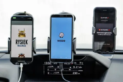 Trzy telefony w uchwytach na desce rozdzielczej: z lewej Rysiek, w środku Waze, a po prawej Yanosik. Którą nawigację wybierzesz?