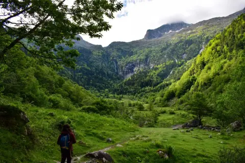 Une randonneuse explore le cirque de Cagateille, un paysage verdoyant de montagnes, de forêts et de cascades.