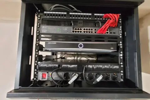 W szafie sieciowej znajduje się router, switch TP-Link, rejestrator Hikvision i listwa zasilająca.