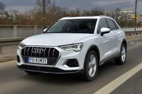 Białe Audi Q3 w ruchu drogowym. Kierowca za kierownicą. Wiele osób szuka audi q3 opinie przed zakupem.