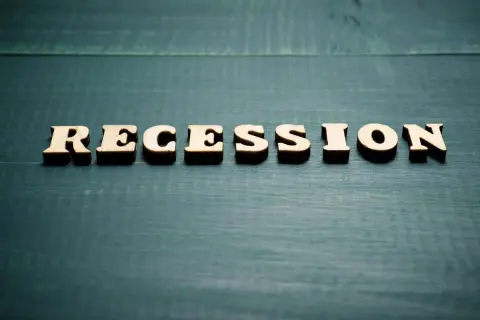 Drewniane litery układają napis "RECESSION". To słowo często pojawia się, gdy zastanawiamy się, co to znaczy recesja i jak wpływa na gospodarkę.