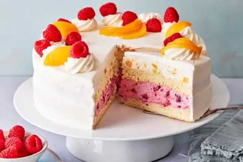 Eine köstliche Pfirsich Melba Torte mit saftigen Himbeeren und Pfirsichstücken, verziert mit Sahnetuffs.