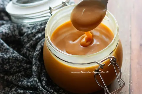 Un cucchiaio raccoglie un denso caramello salato da un barattolo di vetro.