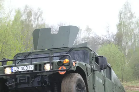 Zielony humvee z tablicą rejestracyjną UB 00317 jedzie przez las.