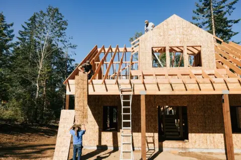Construcción de una casa de madera, con obreros colocando tableros. El proceso de saber cuanto cuesta hacer una casa es complejo.