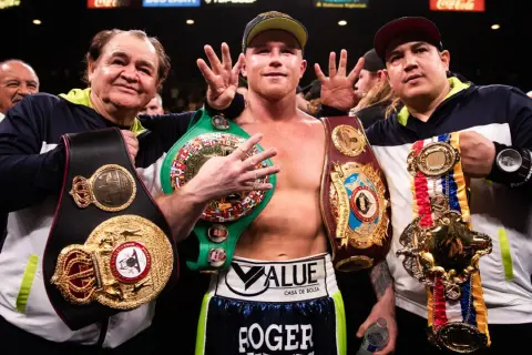 Canelo, flanked by his trainers, proudly displays multiple championship belts, a testament to his incredible win streak.