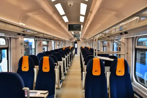 Wnętrze nowoczesnego wagonu PKP Intercity, idealnego na podróż z Poznania do Mielna. Siedzenia w kolorze granatowym z pomarańczowymi zagłówkami.