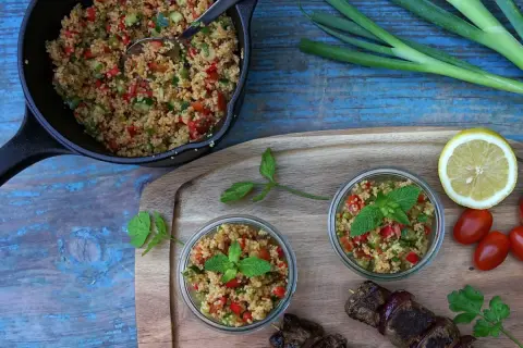 Frischer Couscous-Salat mit Tomaten, Gurken und Minze, serviert in Gläsern und einer Pfanne, daneben ein Spieß mit Fleisch.