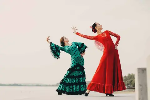 Dos mujeres bailan flamenco. Una con vestido verde de lunares, la otra con rojo. Inspiración para palos del flamenco para niños.