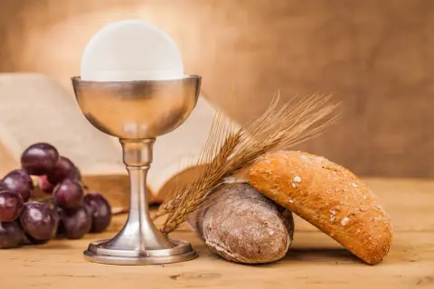 Kielich z hostią, winogrona, chleb i kłosy zbóż – symbole Eucharystii na drewnianym stole.