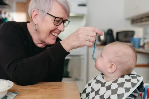Glad mormor matar bebis med smakportioner. Första maten för en 4 månader gammal bebis.
