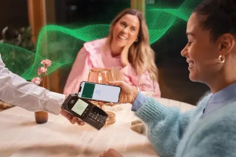 Uśmiechnięte kobiety płacą telefonem w restauracji. Pozytywne fortum opinie o szybkich płatnościach.
