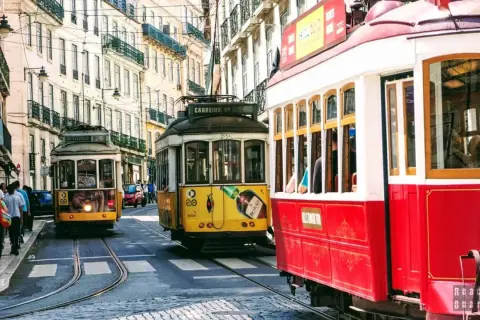 Żółty i czerwony tramwaj w Lizbonie pędzą wąską uliczką między zabytkowymi kamienicami.