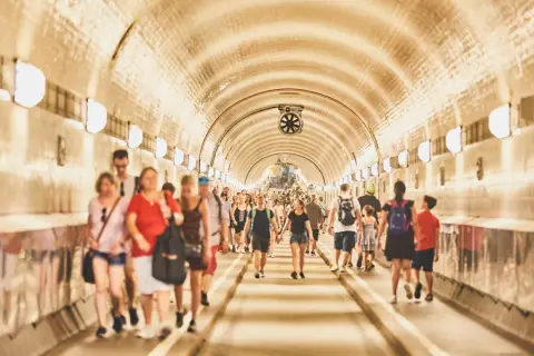 Menschen gehen durch den hell erleuchteten, gewölbten Gang des alten Elbtunnels.