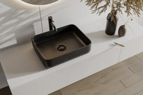 Nowoczesna, ciemna umywalka nablatowa 30x50 z baterią, na białym blacie, obok wazonów z trawą.